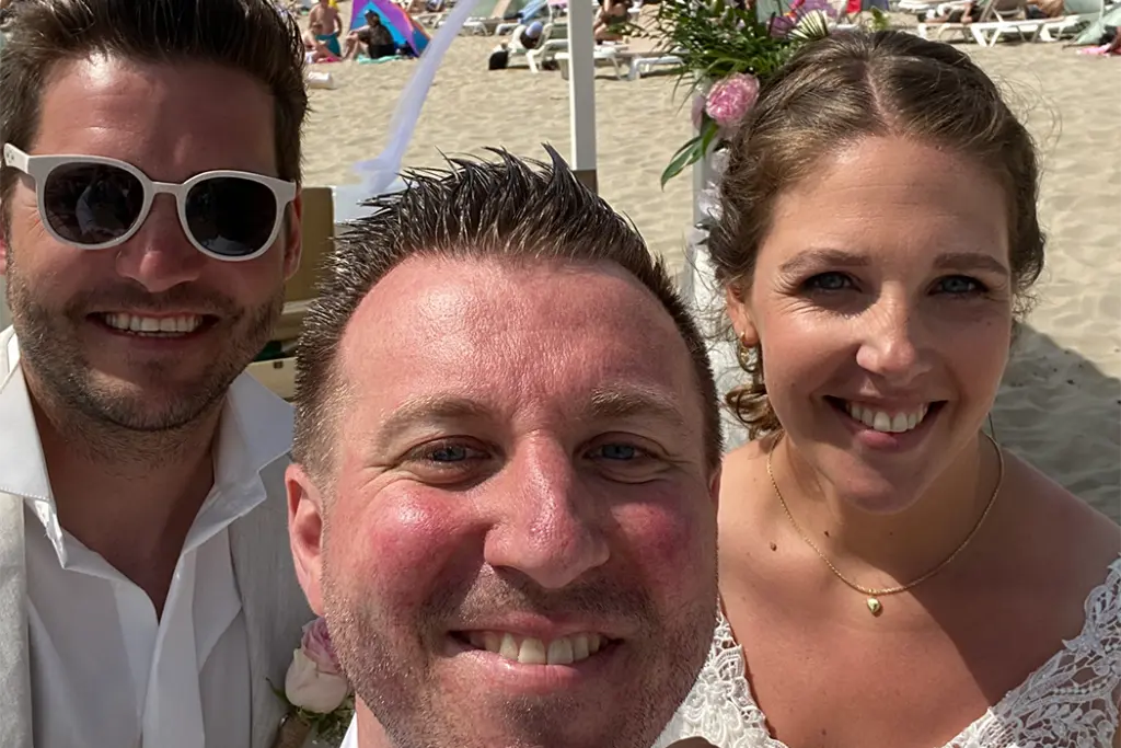 Trauredner macht ein Selfie mit lachendem Brautpaar am Strand